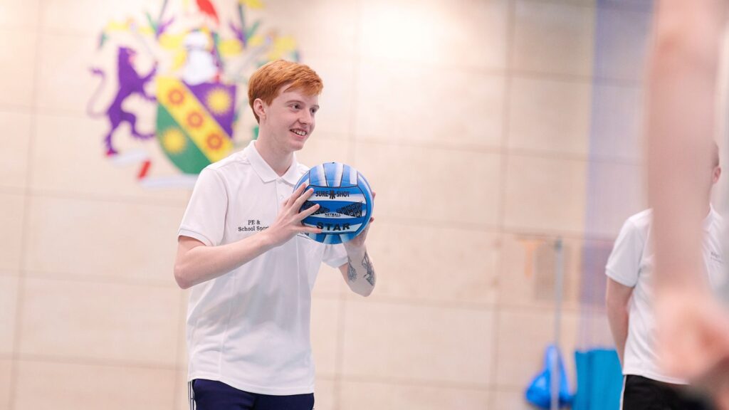 student in PE hall holding football