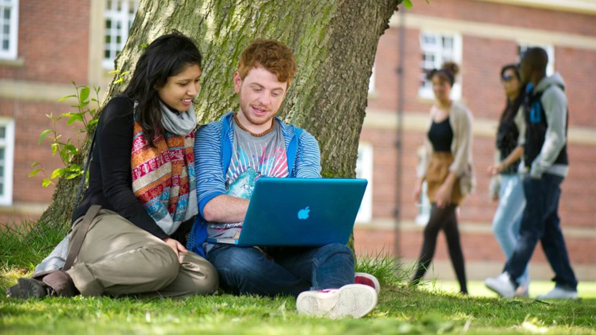 two student sit outside using a laptop