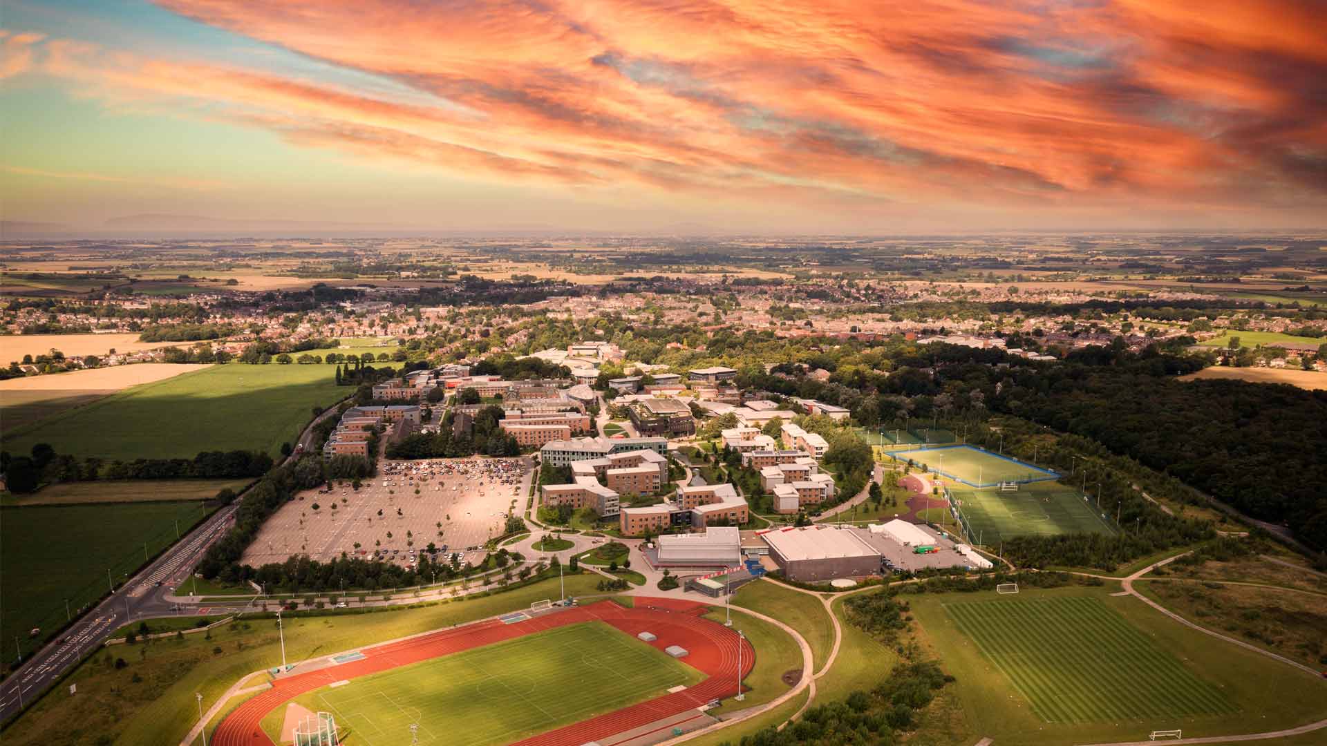 An aerial view of the Eastern Campus at sunset. The running track and grass pitches are visible.