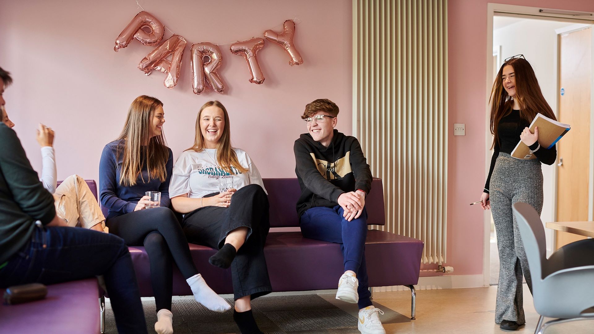 Students talking in their accommodation communal area - Balloons spelling party hand above their head