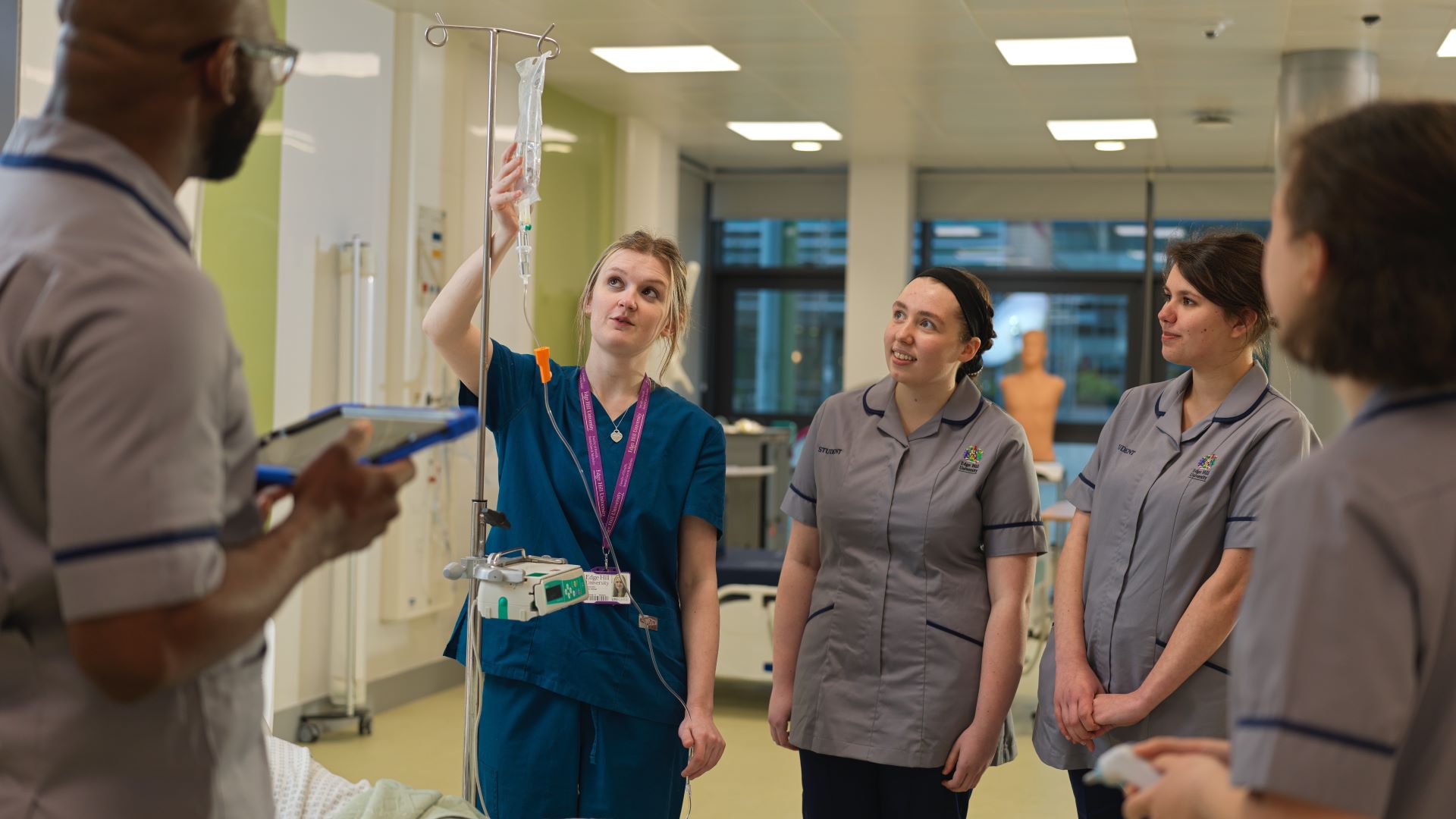 Four student nurses in uniform watch a supervisor set up a drip.