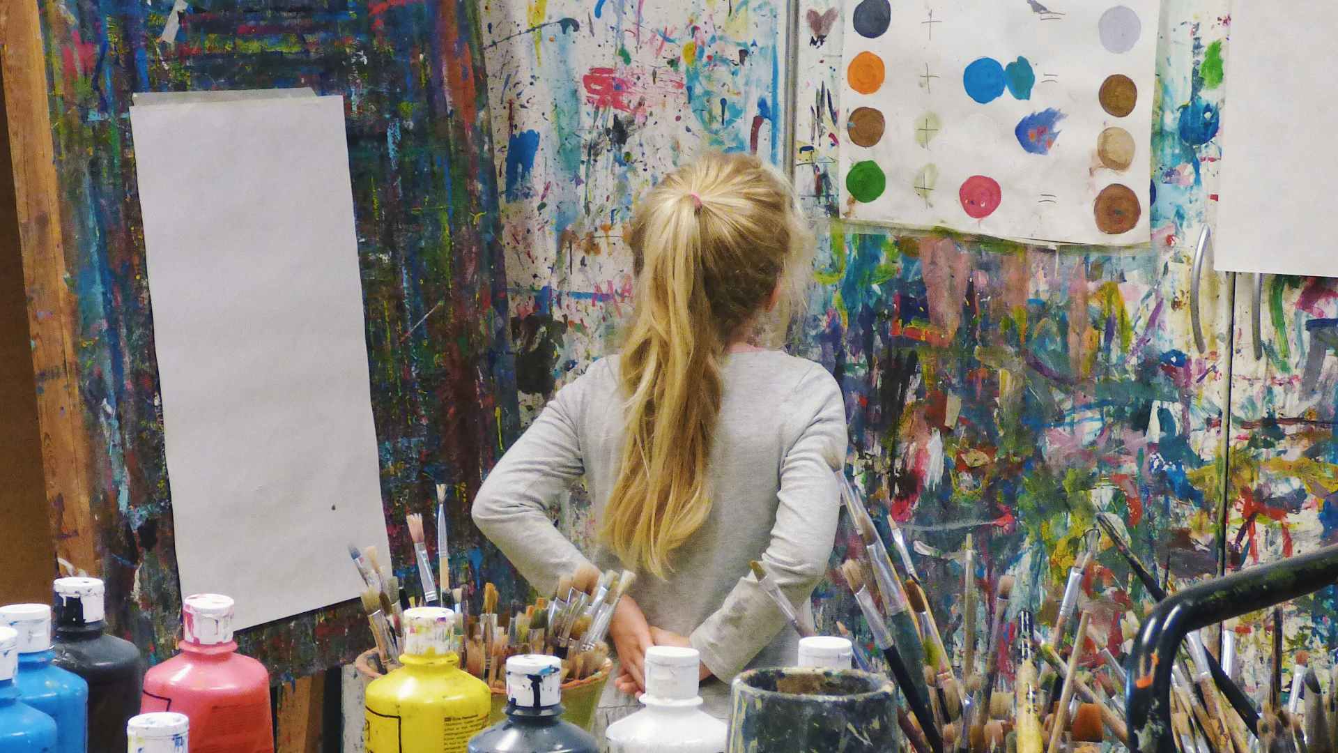 A child looks at her artwork on the wall.