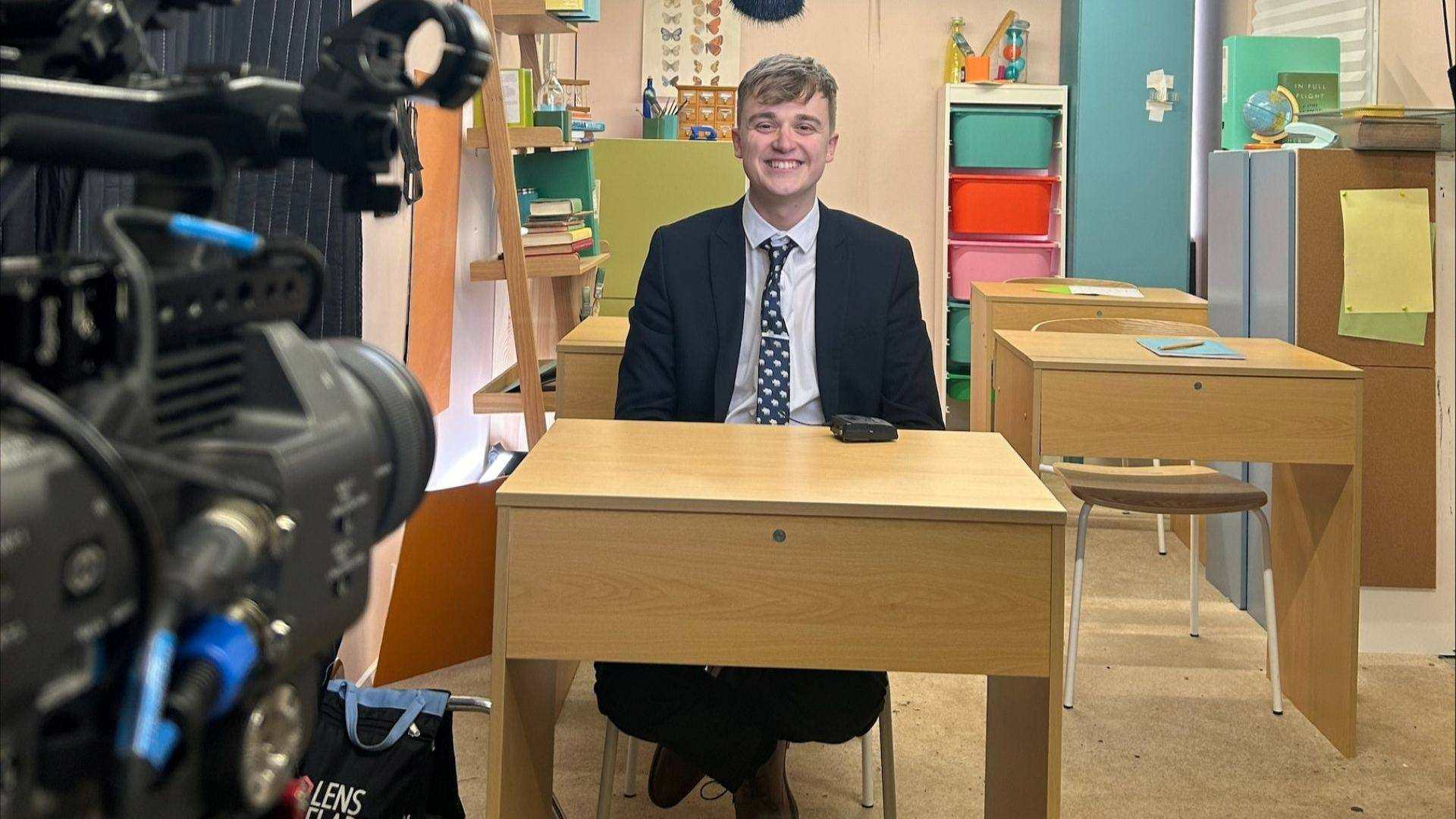 Joshua Geary sat at a school table on set for Educating Yorkshire.